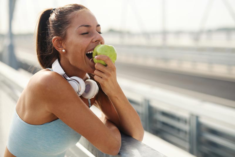 Sportliche Frau beißt genußvoll in einen grünen Apfel Symbol für Heilfasten und Bewegung